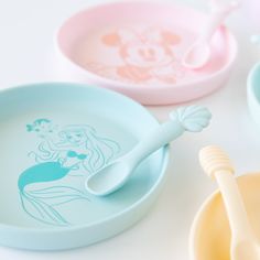 three disney princess plates and spoons on a white table with mickey mouse dishes in the background