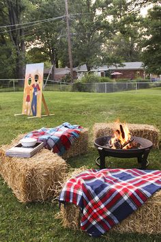 an outdoor fire pit with hay bales and blankets on the ground in front of it