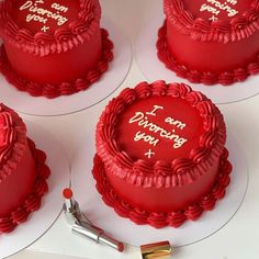 four red cakes sitting on top of white plates with writing on the frosting and icing