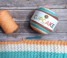 a crochet cupcake next to a ball of yarn on a wooden table