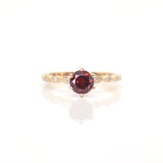 a red and white diamond ring sitting on top of a white surface with the reflection of it