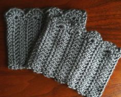 four gray crocheted mittens sitting on top of a wooden table