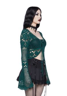 a woman with black hair wearing a green top and fishnet stockings is standing in front of a white background