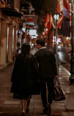 a man and woman walking down the street at night with their back to each other