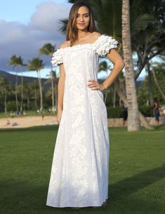 a woman in a white dress standing on the grass with palm trees in the background