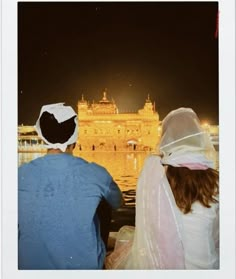 two people looking at the golden temple in amrit, india during night time with bright lights on it