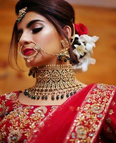 a woman wearing a red and gold bridal outfit with flowers in her hair is looking at the camera