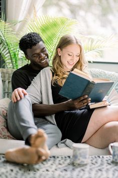 a man and woman sitting on a couch with books in their hands, smiling at each other