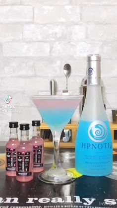 a table topped with bottles of alcohol next to a glass filled with blue liquid and another bottle