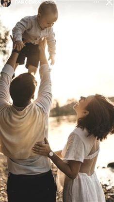 a man holding a baby up in the air while standing next to two other people