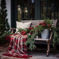 a bench covered in christmas greenery and red berries next to a blanket on the ground