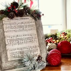 an old sheet music is displayed on a table with pine cones and christmas decorations around it