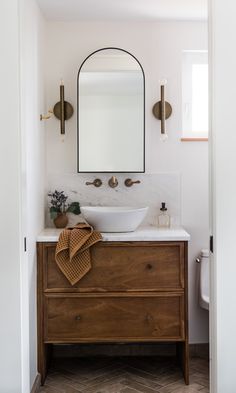 a white sink sitting under a mirror next to a wooden cabinet with a towel on it