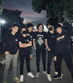 group of young men standing next to each other in front of some trees at night