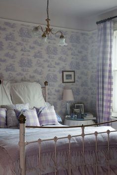 a white bed sitting next to a window in a room with purple and white wallpaper