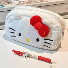 a hello kitty pencil case with a red bow on it and a pen next to it