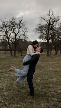 a man holding a woman in his arms while standing on top of a lush green field