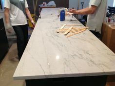 two men are standing at a counter with tools on it and one man is making something