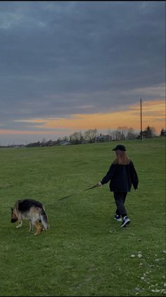 a woman is walking her dog on a leash in the park at sunset or dawn