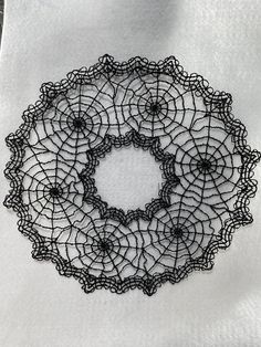 a black doily is sitting on a white tablecloth with an intricate design in the center