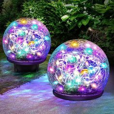 two large glass balls with lights on them sitting in the middle of a garden at night