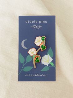 a pin with two flowers on it sitting on top of a white cloth covered sheet