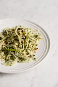 a white plate topped with shredded broccoli on top of a marble countertop