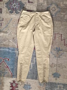 a pair of beige pants with laces on the bottom and side, sitting on a rug