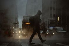 a man walking across a street in the rain with a backpack on his back and cars behind him