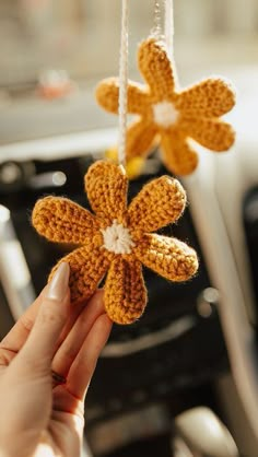 a hand holding a crocheted flower ornament hanging from a car dashboard