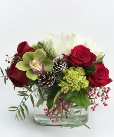 a vase filled with flowers and greenery on top of a white table next to a pine cone