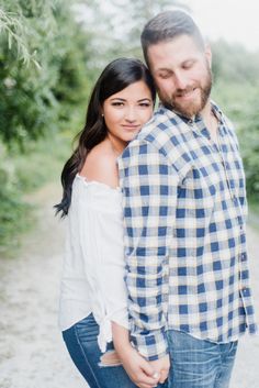 a man and woman standing next to each other on a dirt road with trees in the background