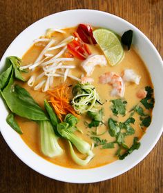 a white bowl filled with soup and garnishes on top of a wooden table