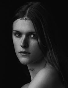 a black and white photo of a woman with tattoos on her chest, looking at the camera