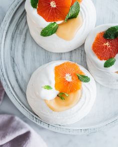 three desserts on a plate with orange slices and mint leaves in the top layer