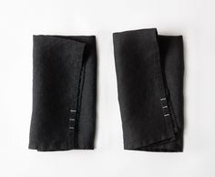 two folded black linen napkins with white stitching on each side and one in the middle