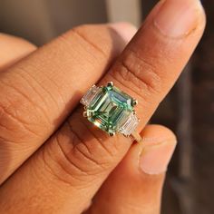 an emerald and diamond ring is being held by someone's hand in front of the camera