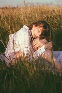 a woman is laying in the grass with her head on her chest and eyes closed