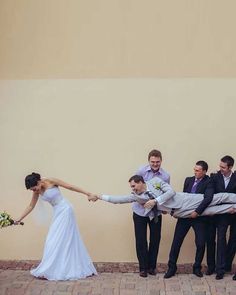 a bride and groom holding hands with their wedding party in front of a tan wall