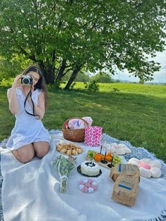 a woman sitting on a blanket with food and a camera in front of her,