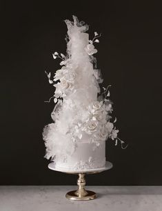 a white wedding cake decorated with flowers and feathers on a silver platter against a black background