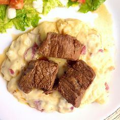 a white plate topped with meat and mashed potatoes covered in gravy next to lettuce