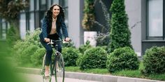 a woman is riding her bike down the street in front of a building with trees and bushes