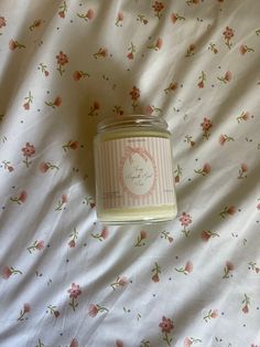 a jar of candle sitting on top of a bed covered in pink flowers and white sheets