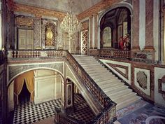 an ornate staircase with chandelier and checkered flooring in a palace like setting