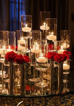 candles and roses are arranged on a glass table in front of a chandelier