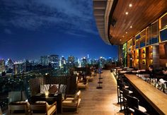 an outdoor bar overlooking the city skyline at night with lots of chairs and tables in front of it