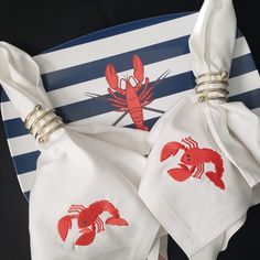 two napkins with lobster embroidered on them are sitting on a striped place mat, next to a blue and white plate