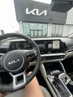 the inside of a car with steering wheel, dashboard and display screen in front of a building