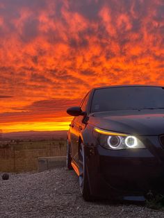 a car parked on the side of a dirt road under a red sky with clouds